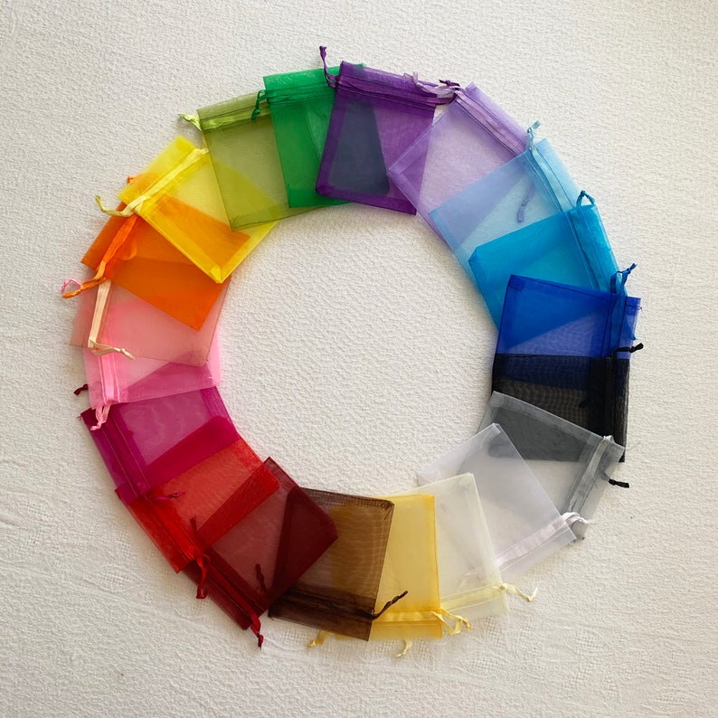 K&ouml;nnte beinhalten: Ein Set mit 18 bunten Organzas&auml;ckchen, die in einem Kreis angeordnet sind. Die S&auml;ckchen bestehen aus durchsichtigem Stoff und sind in verschiedenen Farben erh&auml;ltlich, darunter Rosa, Rot, Orange, Gelb, Gr&uuml;n, Blau, Lila und Schwarz.