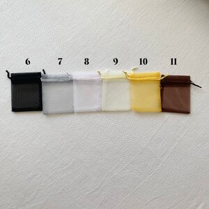 K&ouml;nnte beinhalten: Sechs kleine Organzas&auml;ckchen in verschiedenen Farben, darunter Schwarz, Wei&szlig;, Creme, Gelb und Braun. Die S&auml;ckchen sind von 6 bis 11 nummeriert.