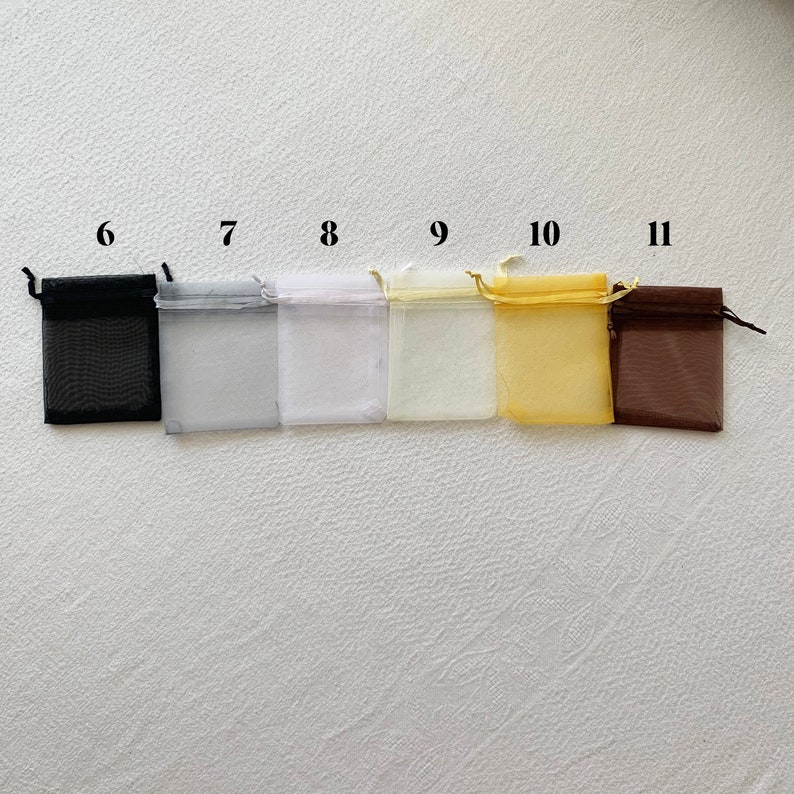 K&ouml;nnte beinhalten: Sechs kleine Organzas&auml;ckchen in verschiedenen Farben, darunter Schwarz, Wei&szlig;, Creme, Gelb und Braun. Die S&auml;ckchen sind von 6 bis 11 nummeriert.