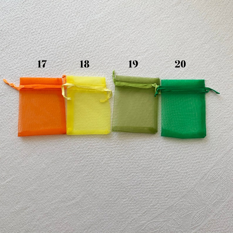 K&ouml;nnte beinhalten: Vier kleine Organzas&auml;ckchen in verschiedenen Farben: orange, gelb, gr&uuml;n und dunkelgr&uuml;n. Die S&auml;ckchen sind mit den Nummern 17, 18, 19 und 20 beschriftet.