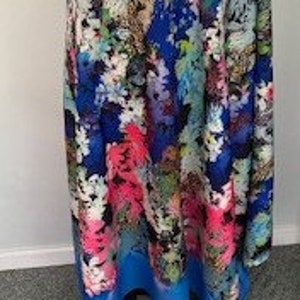 Op de afbeelding: Een blauwe rok met een kleurrijke bloemenprint. De print bevat een verscheidenheid aan bloemen en bladeren in tinten roze, groen, geel en wit.