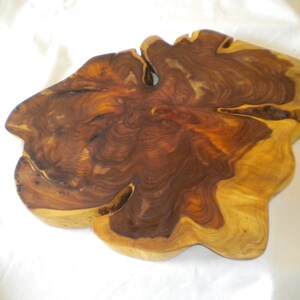 May include: A large, irregularly shaped wooden serving tray with a natural wood finish. The wood grain is visible and has a rich brown color.
