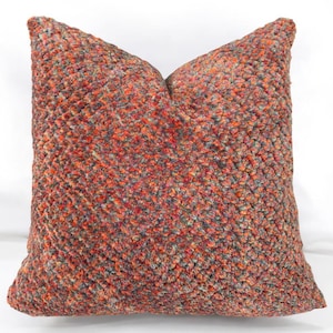 Puede incluir: Una almohada decorativa con una tela texturizada multicolor. La tela es una mezcla de naranja, rojo, gris y azul.