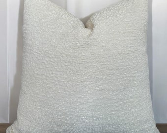 Puede incluir: Una almohada de textura blanca con un brillo sutil. La almohada es cuadrada y tiene un diseño simple.