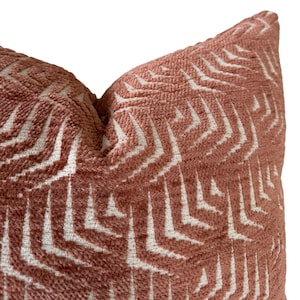 Puede incluir: Primer plano de una almohada de tiro de color rosa y blanco con estampado. La almohada tiene un diseño geométrico con un brillo sutil.