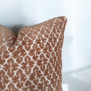 Puede incluir: Una almohada de tiro de color marrón y blanco con una textura suave y aterciopelada.