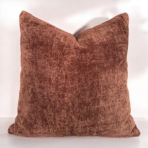 Peut inclure: Un oreiller en peluche marron avec une texture douce et duveteuse. L'oreiller est de forme carr&eacute;e et a un design simple.