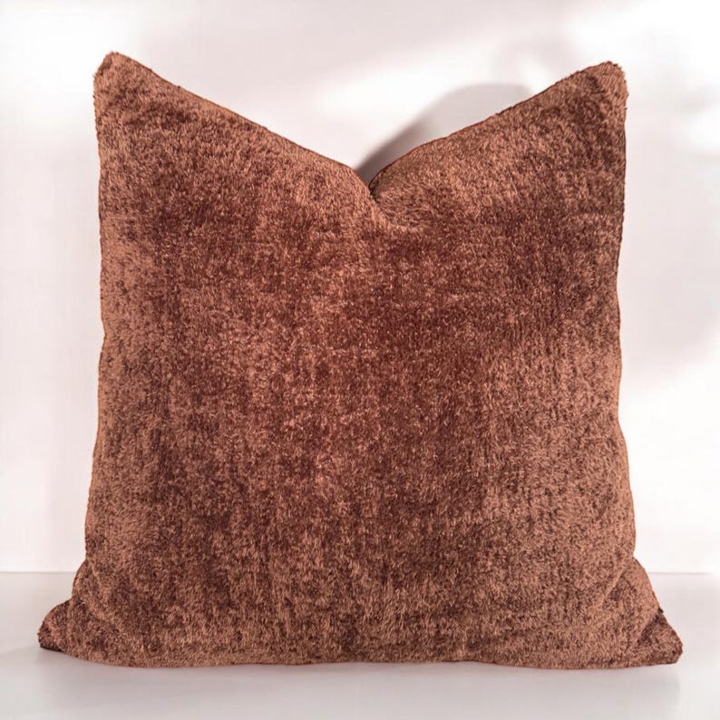 Peut inclure: Un oreiller en peluche marron avec une texture douce et duveteuse. L'oreiller est de forme carr&eacute;e et a un design simple.