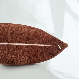 Peut inclure: Un oreiller en peluche marron avec une fermeture &eacute;clair blanche. L'oreiller est doux et moelleux.