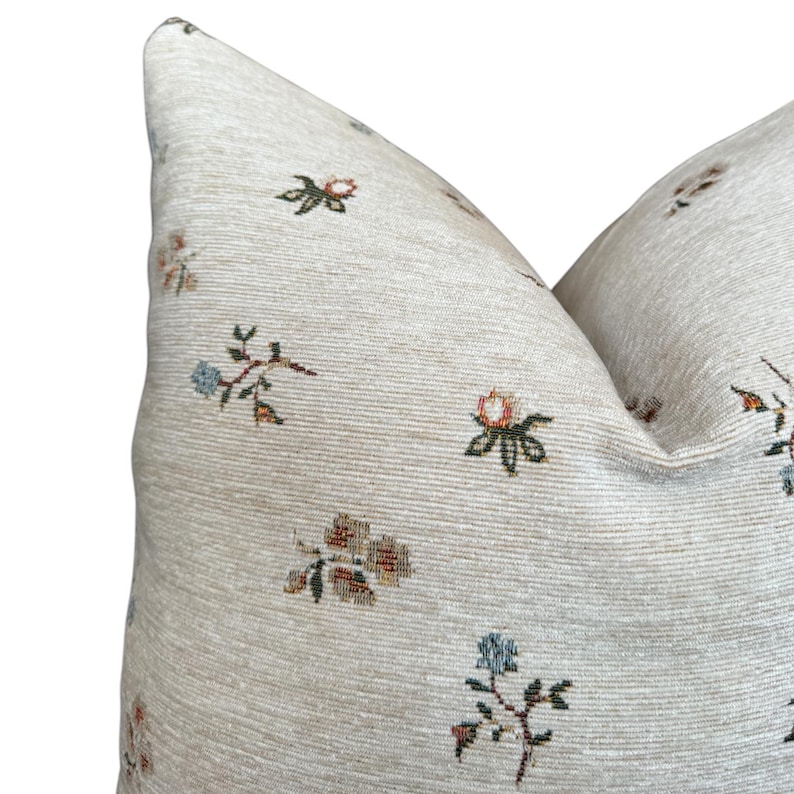 May include: Close-up of a beige pillow with a floral pattern. The pillow has a subtle texture and features small, multi-colored flowers.