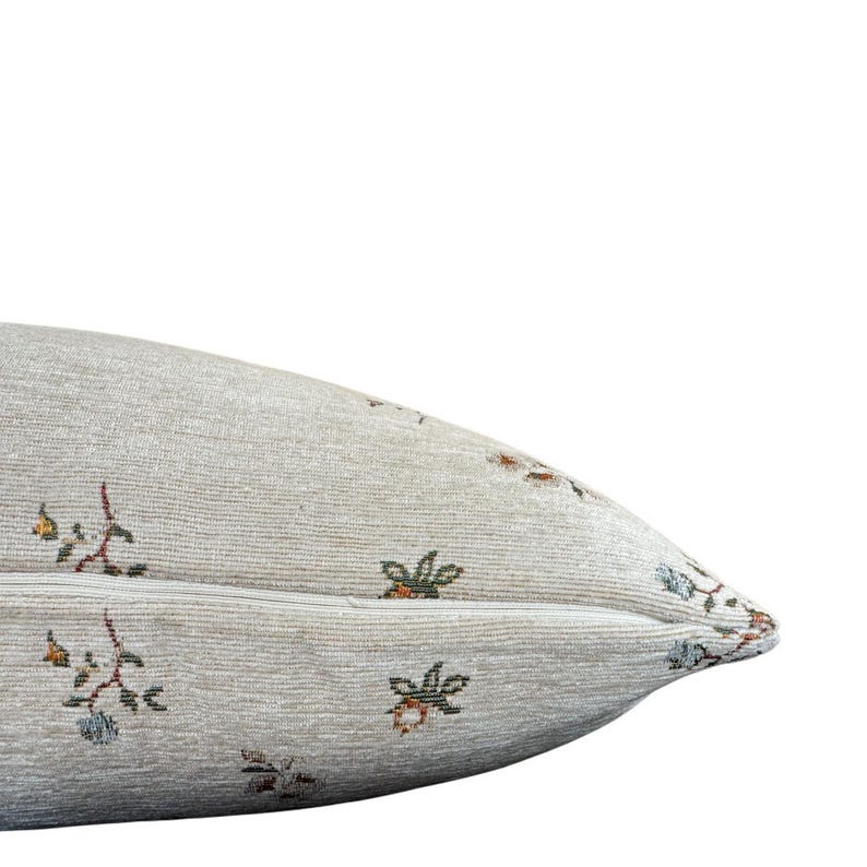 May include: A beige pillow with a floral pattern. The pillow has a zipper closure and is made of a soft, textured fabric.
