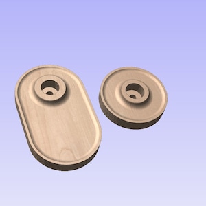 Op de afbeelding: Twee onafgewerkte houten componenten. Eén is ovaal van vorm met een centrale cirkelvormige inkeping en een gat. De andere is cirkelvormig met een vergelijkbaar ontwerp. Beide zijn lichtbruin en lijken te zijn gesneden of machinaal bewerkt.