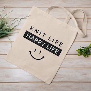 Tote bag with wood plank back drop.  Tote bag says "knit life happy life"