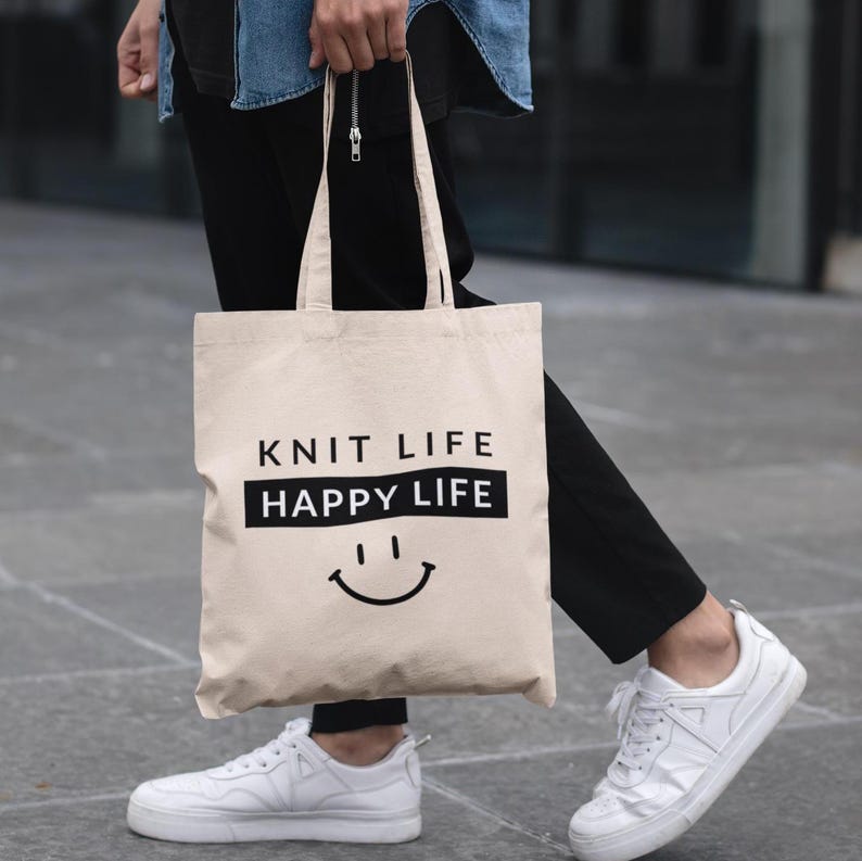 Natural Cotton Canvas Knitting Project Tote - 15x16 inches.  Woman wearing black pants, blue shirt and white sneakers carrying a cotton canvas bag that says Knit Life Happy Life.