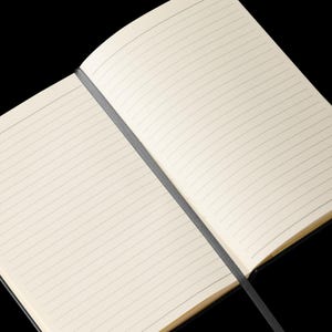 May include: An open lined notebook with a black cover. The notebook is lying flat on a black surface.
