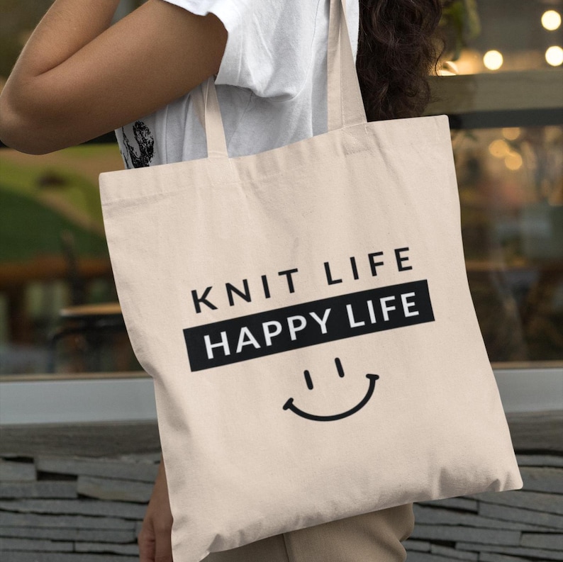 Woman holding tote bag on her shoulder that says "Knit Life Happy Life"