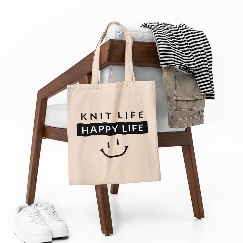Tote bag hanging on a chair with clothes laid out, bag says "Knit Life Happy Life"