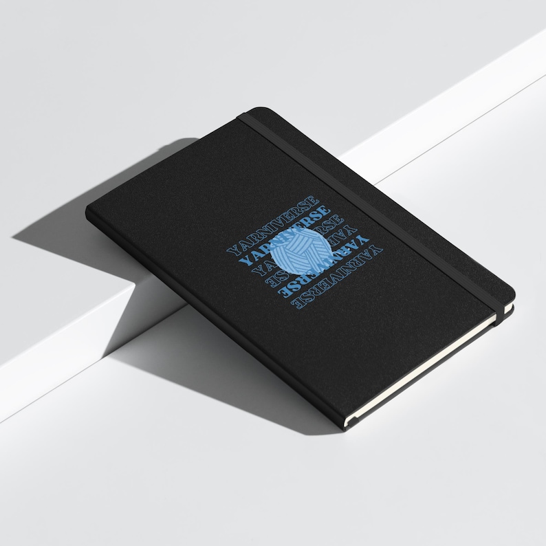 May include: Black notebook with a blue yarn ball graphic and the text "Yarn Universe" repeated in a circular pattern.