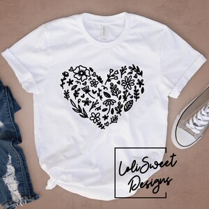 Peut inclure: T-shirt blanc avec un motif de cœur floral noir. Le motif est composé de petites fleurs, de feuilles et de tiges. Le texte "Loli Sweet Designs" est imprimé en noir au bas du t-shirt.