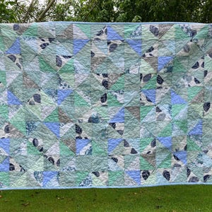 May include: A rectangular quilt featuring a patchwork design of half-square triangles in shades of light blue, sage green, white, and dark grey. The fabric patterns include various botanical leaf prints, subtle geometric grids, and solid colours.