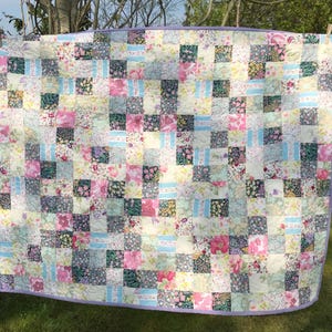 May include: A patchwork quilt with a floral pattern in shades of pink, blue, and green. The quilt is hanging on a washing line outdoors.