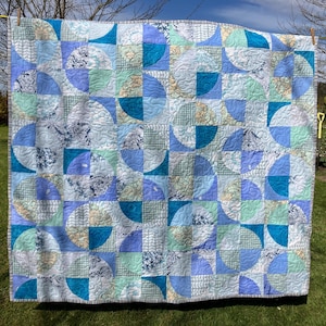 May include: A blue and white quilt with a geometric pattern of semi-circles. The quilt is made from different fabrics with various patterns, including a map print, a floral print, and a solid blue print.