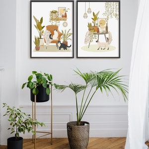 May include: Two framed art prints depict interior scenes with cats, plants, and furniture. One print shows a cat on a chair, the other a cat near a table. The image also includes potted plants and a gold plant stand.
