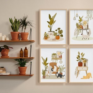 May include: Four framed art prints featuring illustrations of cats in cozy indoor settings with plants. The prints have a neutral color palette with shades of green, brown, and beige. Wooden shelves with potted plants and candles are also visible.