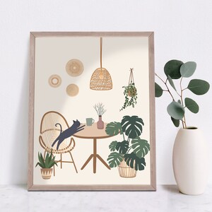 May include: A framed art print featuring a whimsical interior scene. A black cat stretches on a woven chair at a round table. The room includes potted plants, a hanging light, and decorative wall accents. The color palette is neutral with green and brown accents.
