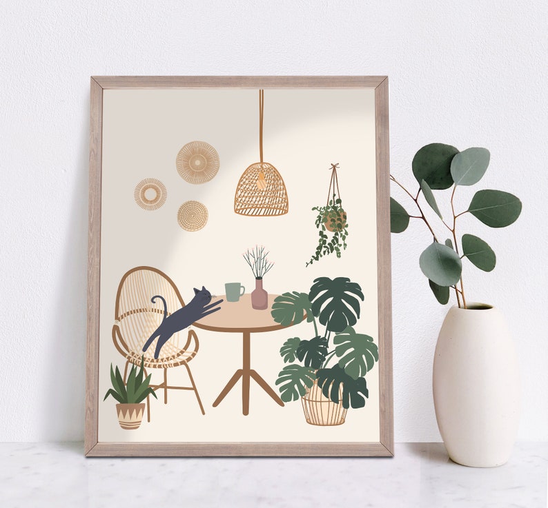 May include: A framed art print featuring a whimsical interior scene. A black cat stretches on a woven chair at a round table. The room includes potted plants, a hanging light, and decorative wall accents. The color palette is neutral with green and brown accents.