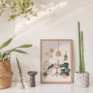 May include: A framed print with a cat leaping over a table, surrounded by plants and a woven lamp. The print is in a light wood frame. A tall cactus in a concrete pot is on the right. Other plants are in woven baskets and glass vases.