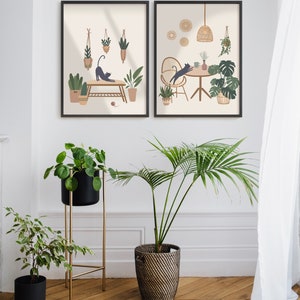 May include: Two framed art prints with black frames depict cats and plants in a minimalist style. The prints are displayed above a collection of potted plants, including a palm and a plant in a black pot on a gold stand. The room has a wooden floor.