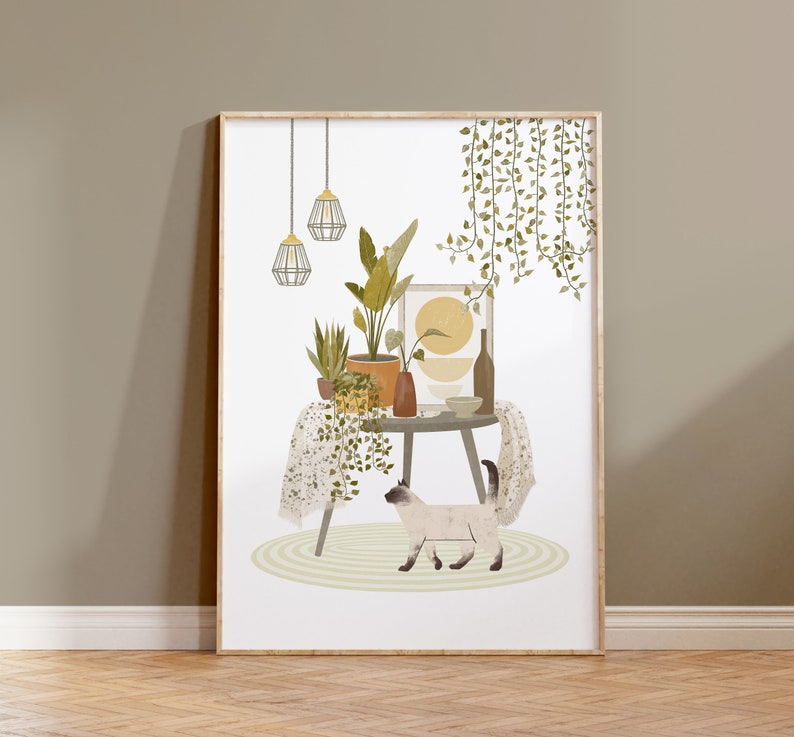 May include: A framed art print featuring a cozy interior scene. A round table displays potted plants, a vase, and a framed artwork. A Siamese cat walks on a rug in front of the table. The print has a neutral color palette with green and yellow accents.