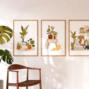 May include: Three framed art prints featuring illustrations of cats and plants. One print shows a cat sitting among potted plants. Another depicts a cat stretching near a nightstand with a plant. The third print shows cats on a chair surrounded by plants.