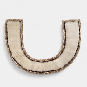 May include: A U-shaped collar with a cream-colored, fluffy interior. The collar is trimmed with a thin black border and a row of small, gold-colored beads. The item is likely a fashion accessory.