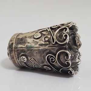 May include: A silver thimble with intricate floral designs and a textured surface.