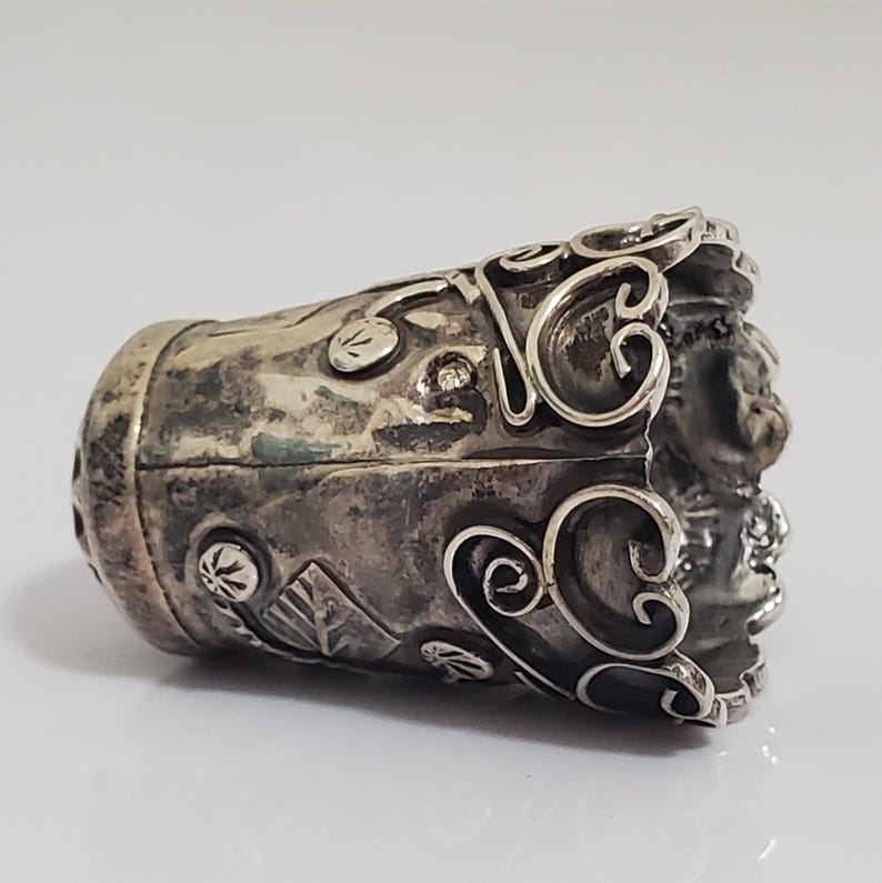 May include: A silver thimble with intricate floral designs and a textured surface.