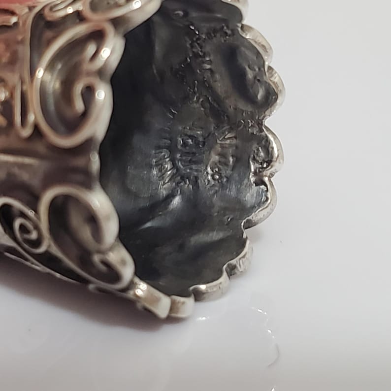 May include: Close-up of the bottom of a silver thimble with an ornate design. The thimble has a maker's mark that reads "STERLING 925".