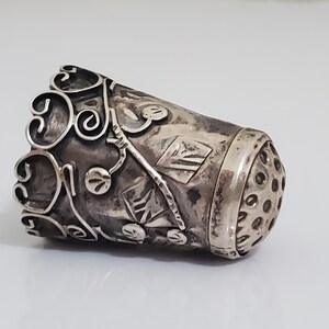 May include: A silver thimble with an intricate floral design and a perforated top.