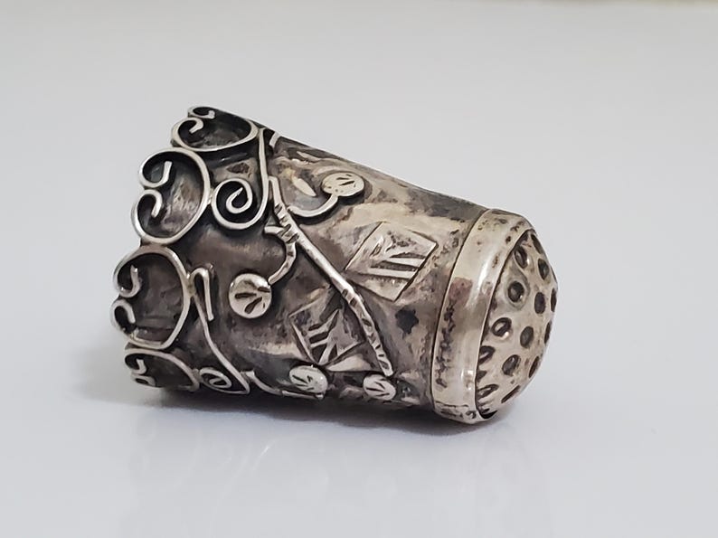 May include: A silver thimble with an intricate floral design and a perforated top.