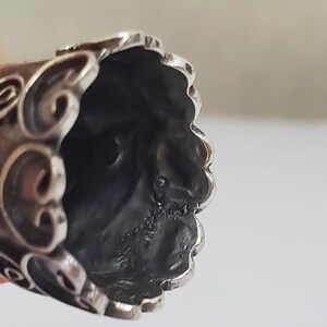 May include: Silver thimble with an ornate design. The inside of the thimble is visible, showing a smooth, silver surface.
