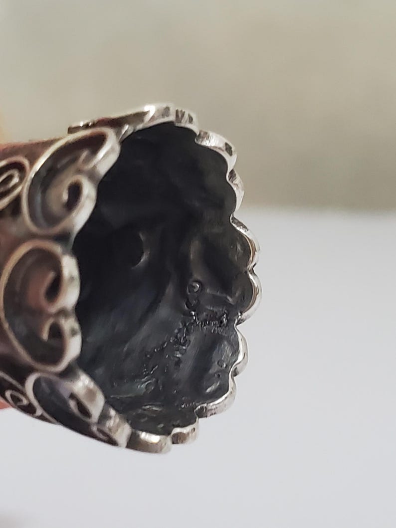 May include: Silver thimble with an ornate design. The inside of the thimble is visible, showing a smooth, silver surface.