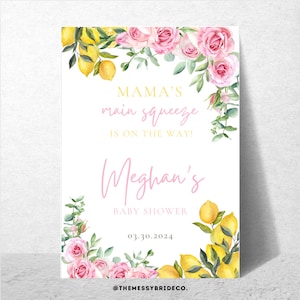 May include: A baby shower sign with a white backdrop, featuring watercolor lemons and pink roses. The sign displays the text "MAMA'S main squeeze IS ON THE WAY!" and "Meghan's BABY SHOWER 03.30.2024". The sign is from @THEMESSYBRIDECO.