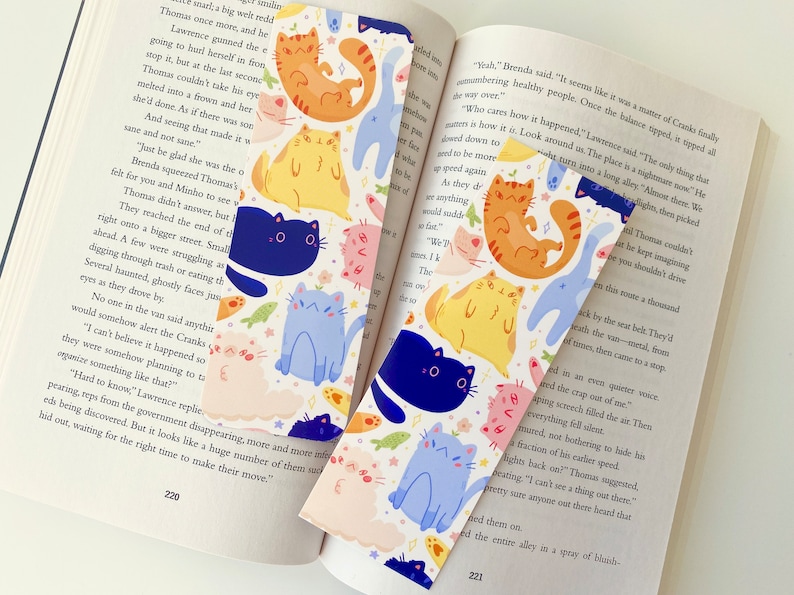 May include: Two colorful bookmarks featuring a repeating pattern of cute cartoon cats in various colors and poses. The cats are surrounded by stars and fish. The bookmarks are perfect for book lovers who want to add a touch of whimsy to their reading experience.