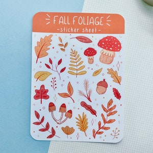 May include: A sticker sheet featuring a fall foliage theme. It includes a variety of autumn leaves, mushrooms and acorns in shades of red, orange and yellow. The sheet is titled "Fall Foliage - sticker sheet -."