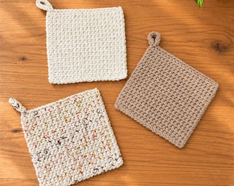 May include: Three square crochet potholders with hanging loops. One is solid off-white, one is solid light brown, and one is a speckled off-white yarn with small flecks of red, yellow, and dark brown throughout the textured stitch pattern.