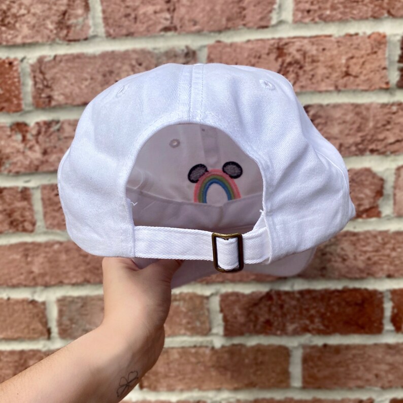 May include: White baseball cap with an embroidered rainbow and Mickey Mouse ears on the back.