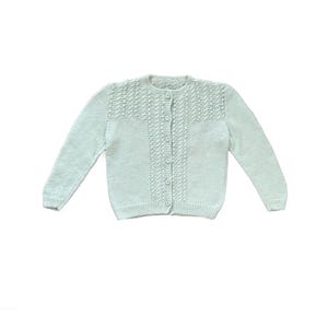 May include: A light blue knitted cardigan with a round neckline and long sleeves. The front features a button-up closure and a textured pattern across the chest. The cardigan is made of a soft, lightweight material, perfect for layering.