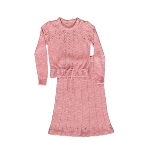 May include: A two-piece, light pink knit outfit. The long-sleeved top has a round neckline and a drawstring waist. The matching skirt is knee-length. Both pieces have a delicate, open-knit design.