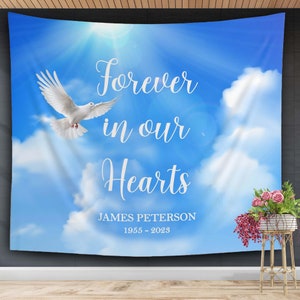 May include: A white dove flies against a blue sky with white clouds. The text "Forever in our Hearts" is written in white cursive font. Below the text is "JAMES PETERSON 1955 - 2023".